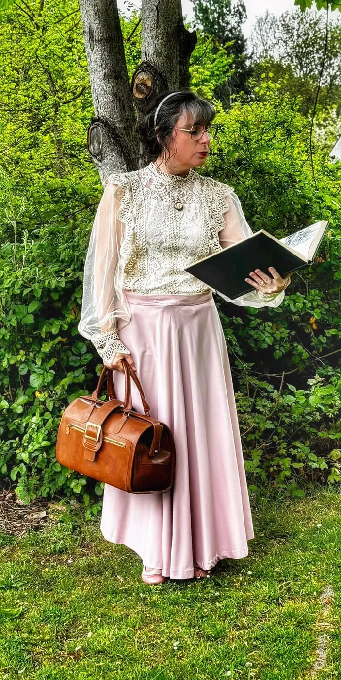 Dorothée en costume des années 1920, un carnet à la main et une valise en cuir, au pied d’un arbre